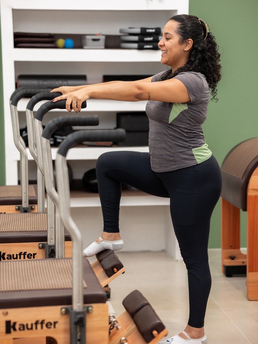 Paciente sorrindo durante exercício no Chair, com estante de acessórios ao fundo