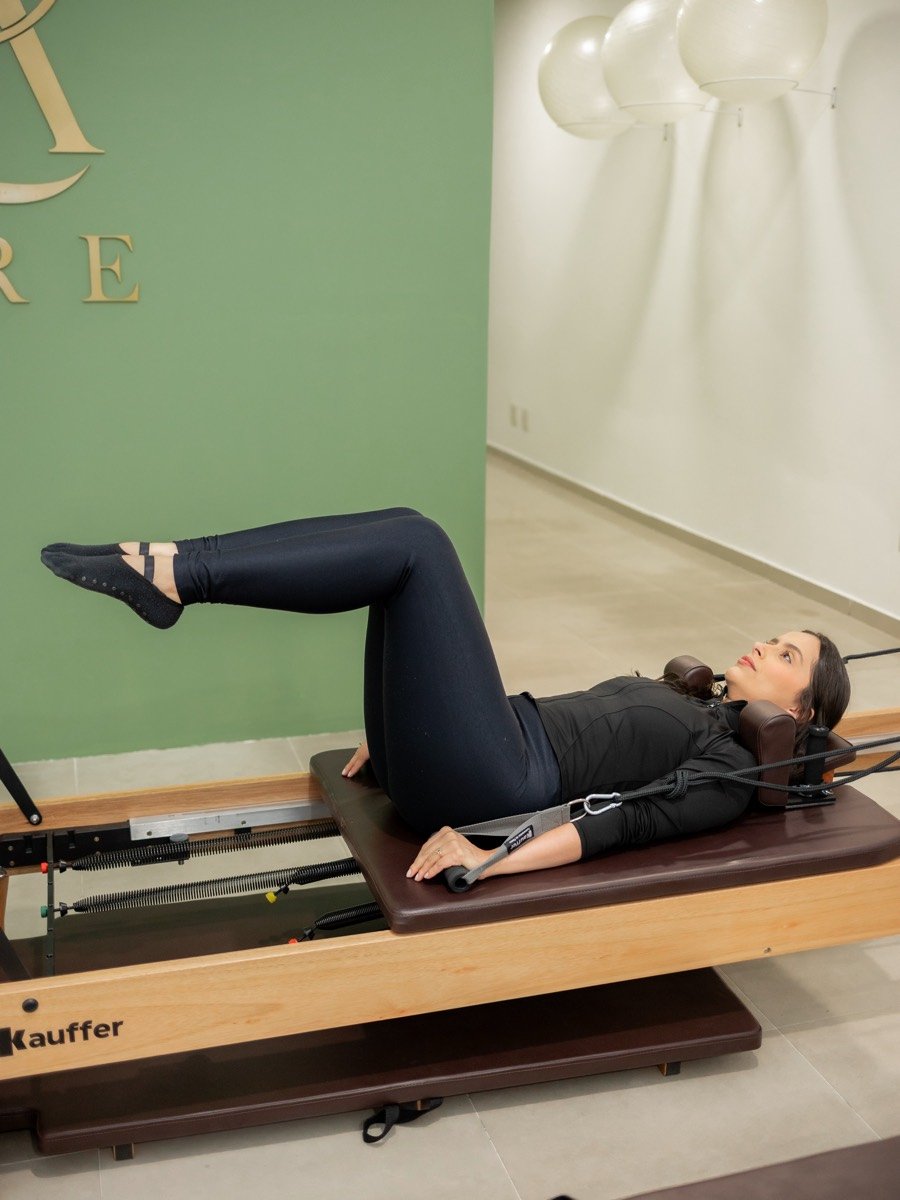 Aluna deitada no Reformer fazendo exercício com as alças